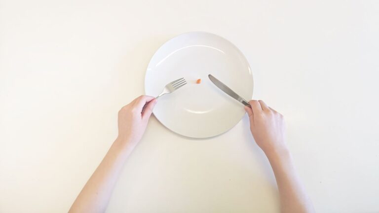 A Person Holding A Fork And Knife Over A Plate