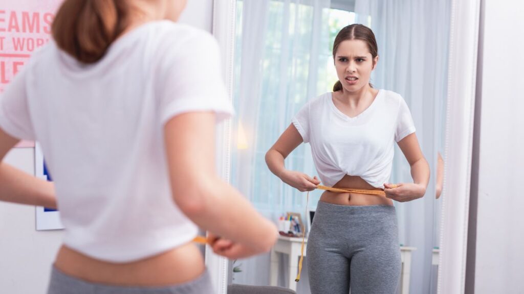 Woman Measuring Her Waist In The Mirror And Looking Concerned